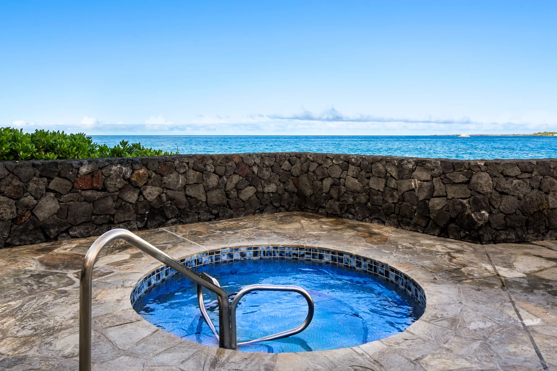 Una pequeña piscina circular está en un patio de piedra junto a un muro bajo, con el océano al fondo.