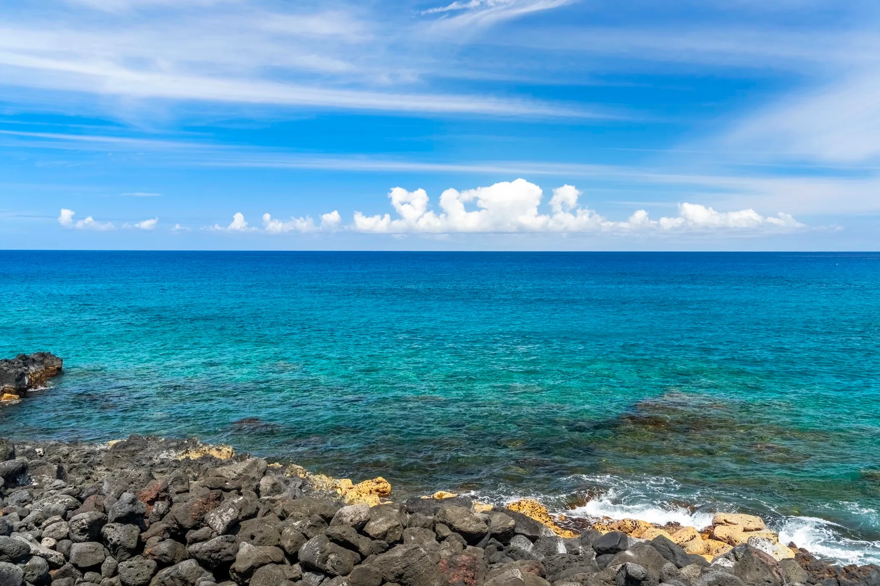 Una costa rocosa bordea aguas turquesas y claras bajo un cielo azul.