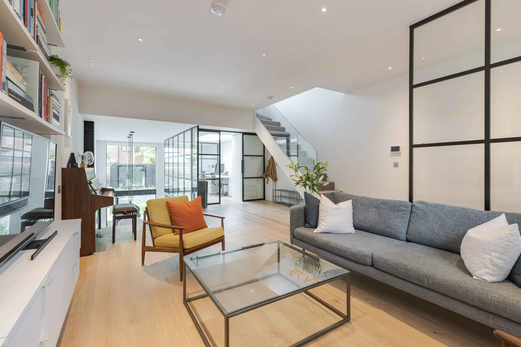 A bright living room with a gray sofa and glass coffee table.
