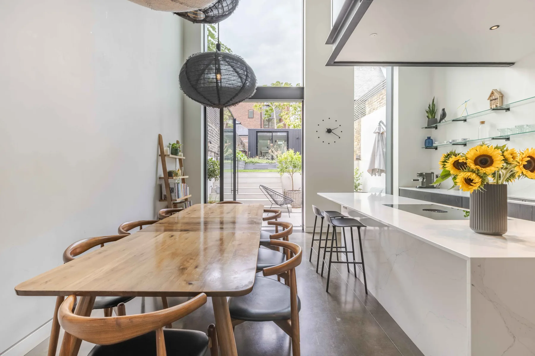 Un comedor luminoso con una larga mesa de madera junto a una isla de cocina blanca.