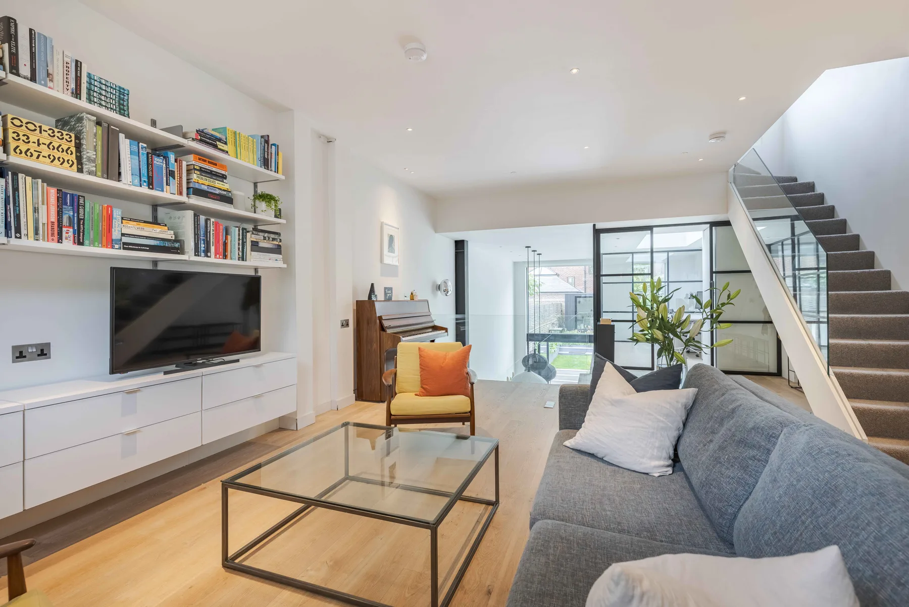 A bright living room with seating, a television, and a staircase.