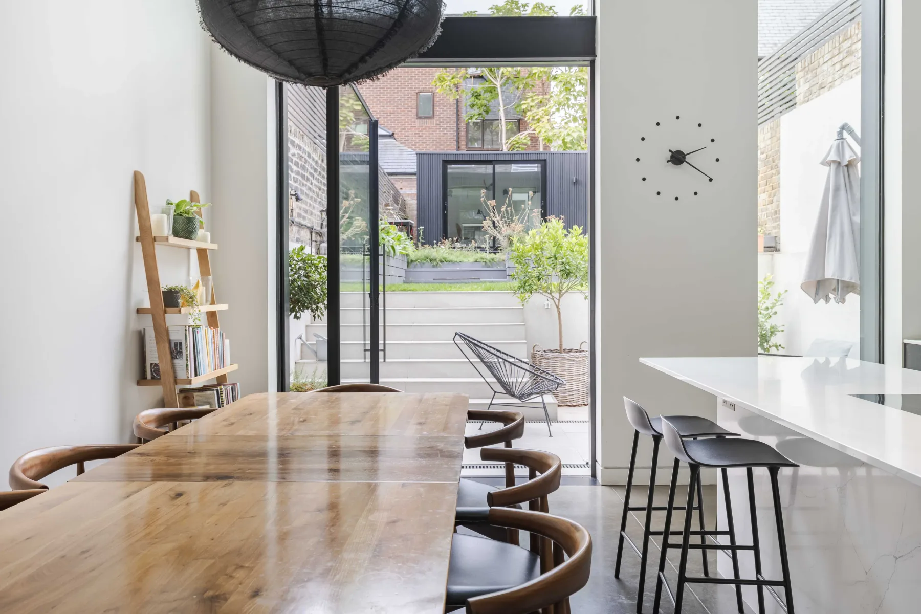 Comedor con una mesa de madera y asientos de bar junto a grandes ventanas.