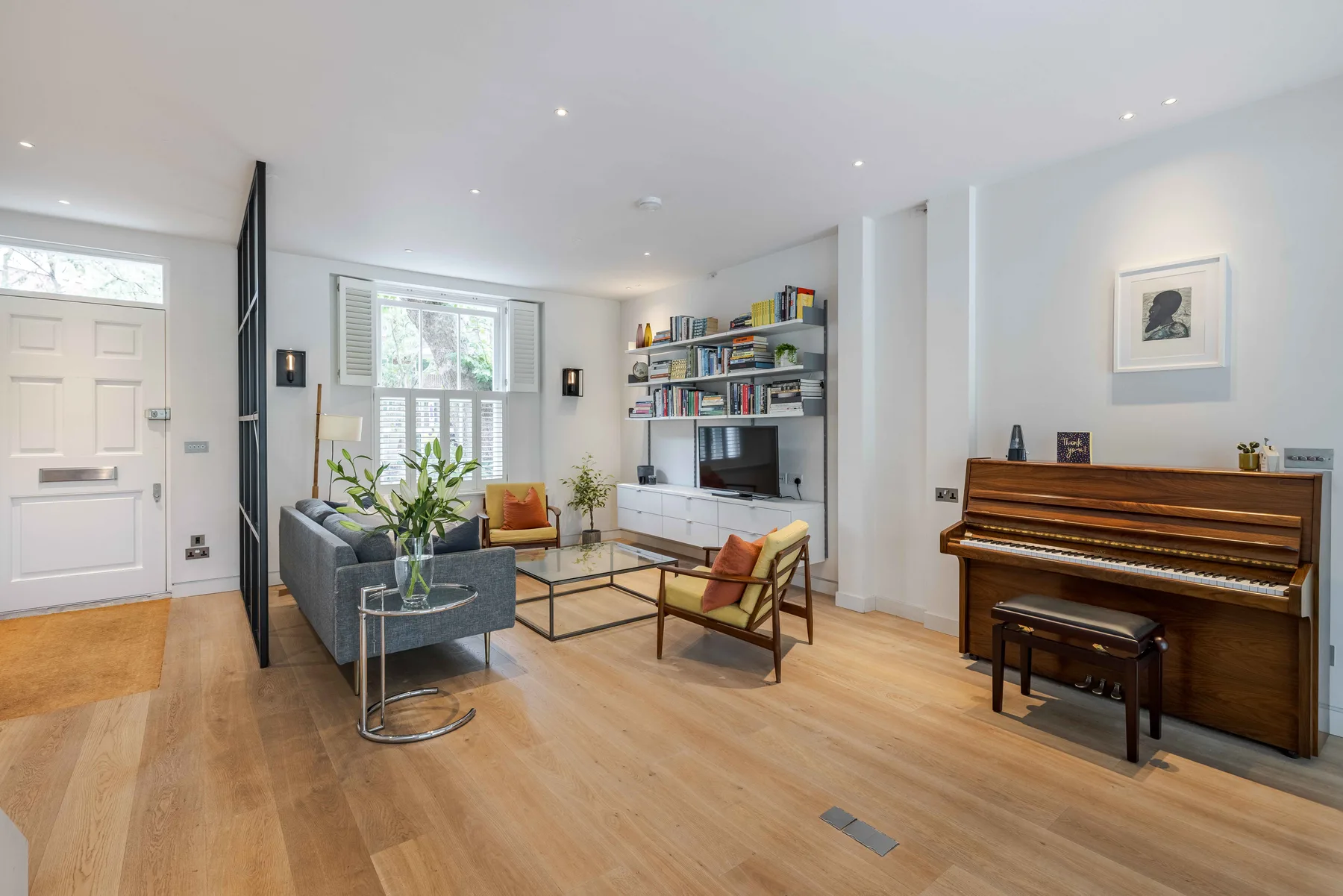 Una sala luminosa tiene asientos, estantes y un piano.