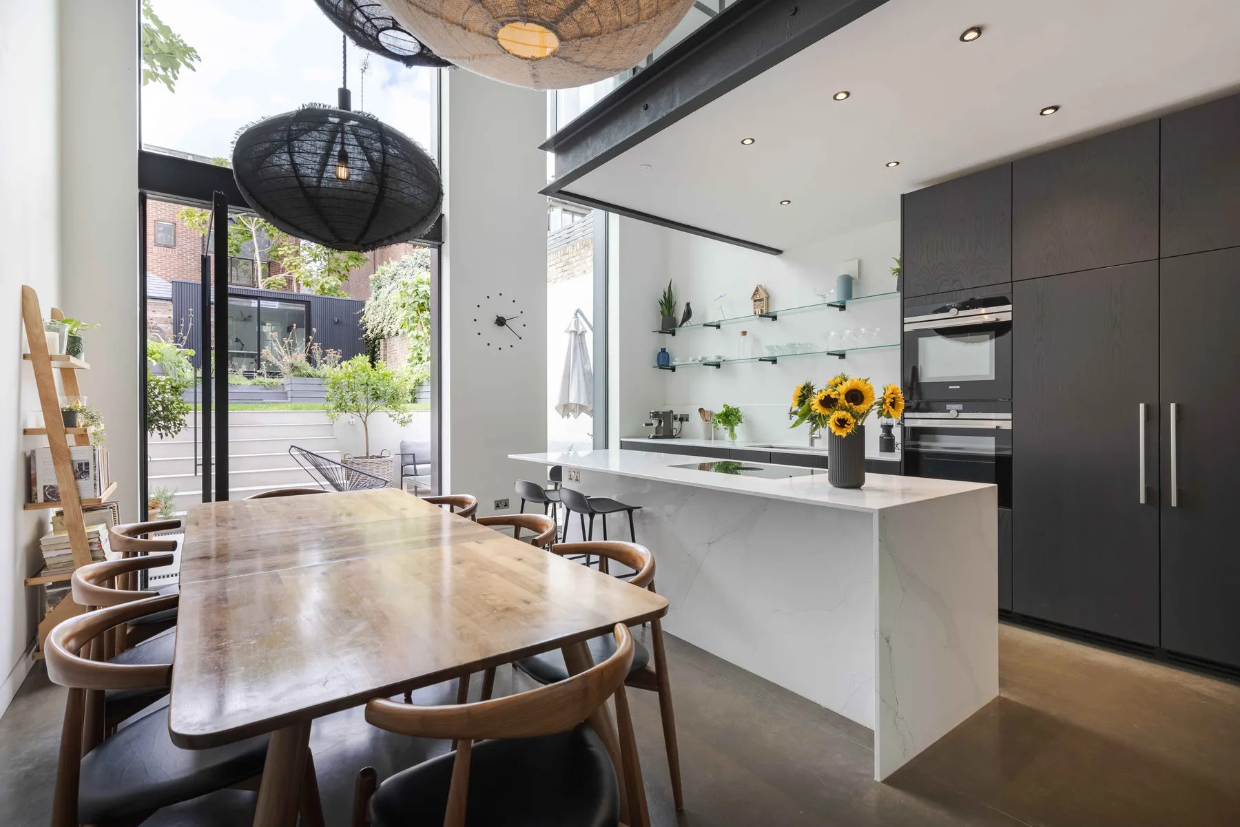 A modern kitchen and dining area with a long table beside large glass doors.