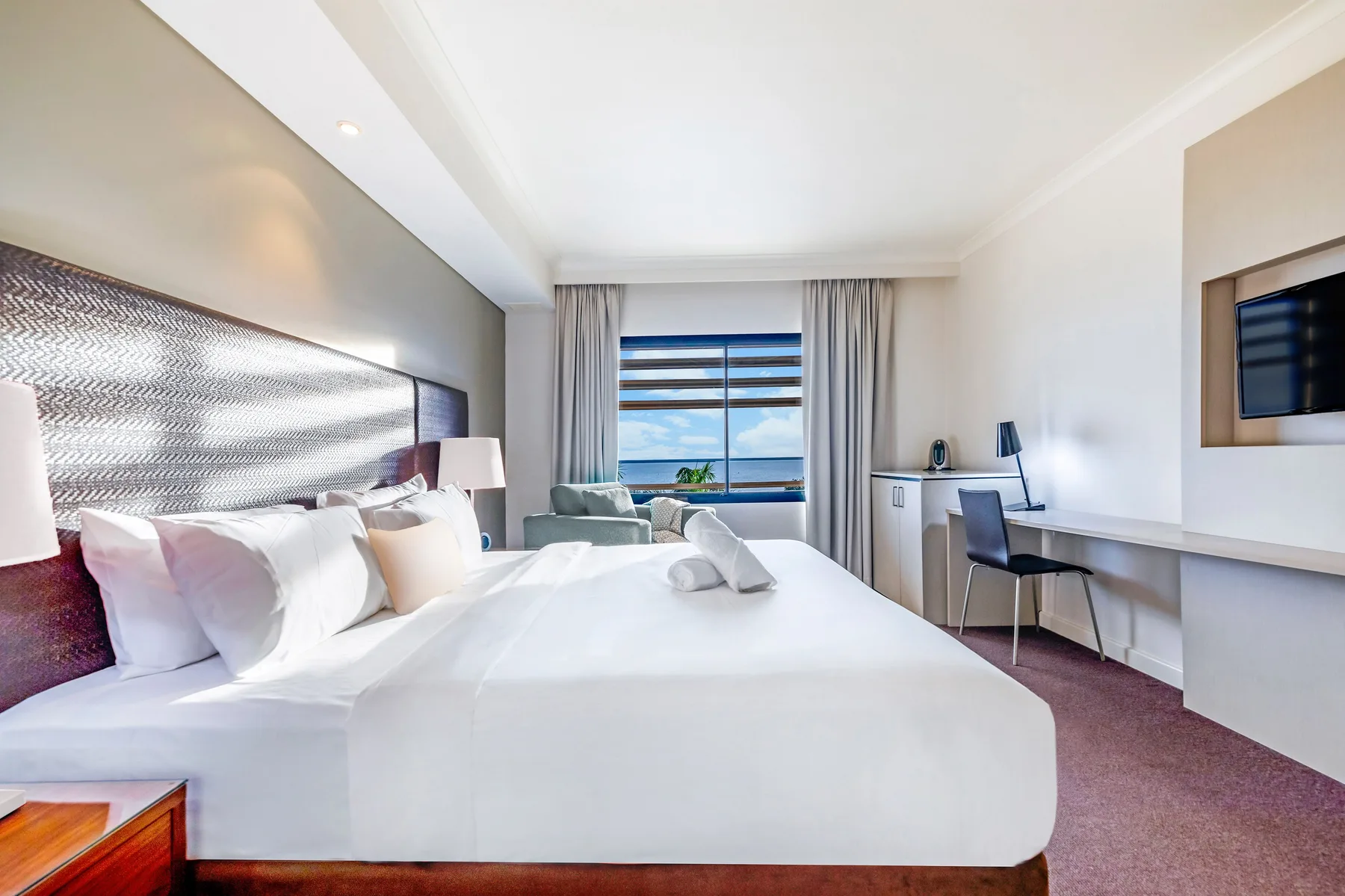 Un dormitorio luminoso con una cama grande, un escritorio y una ventana con vistas al agua.