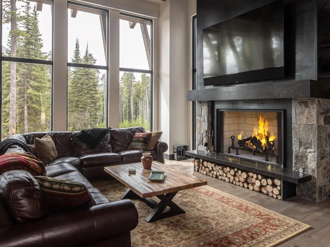Una sala de estar con asientos de cuero, una mesa de centro y una chimenea bajo grandes ventanas.