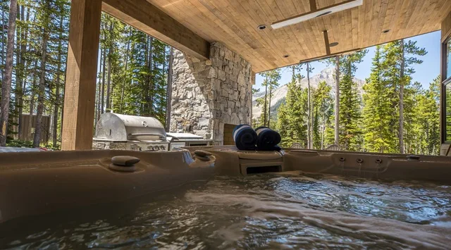 Una bañera de hidromasaje al aire libre está bajo un patio cubierto de madera, frente a los árboles.