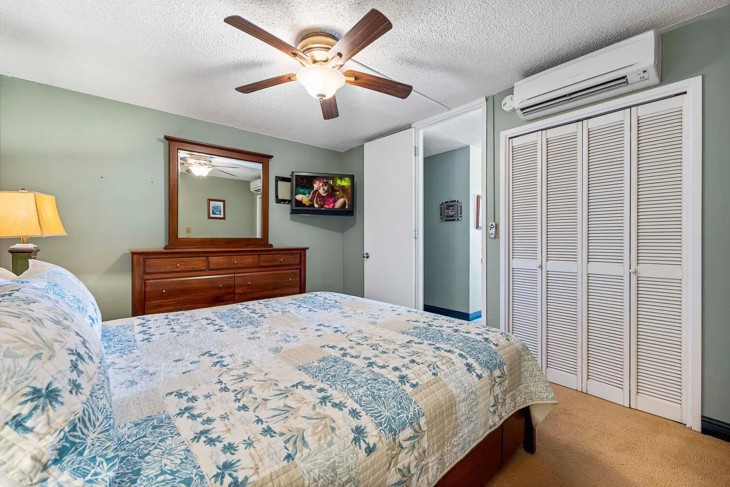 Un dormitorio con una colcha floral, una cómoda de madera y un ventilador de techo.