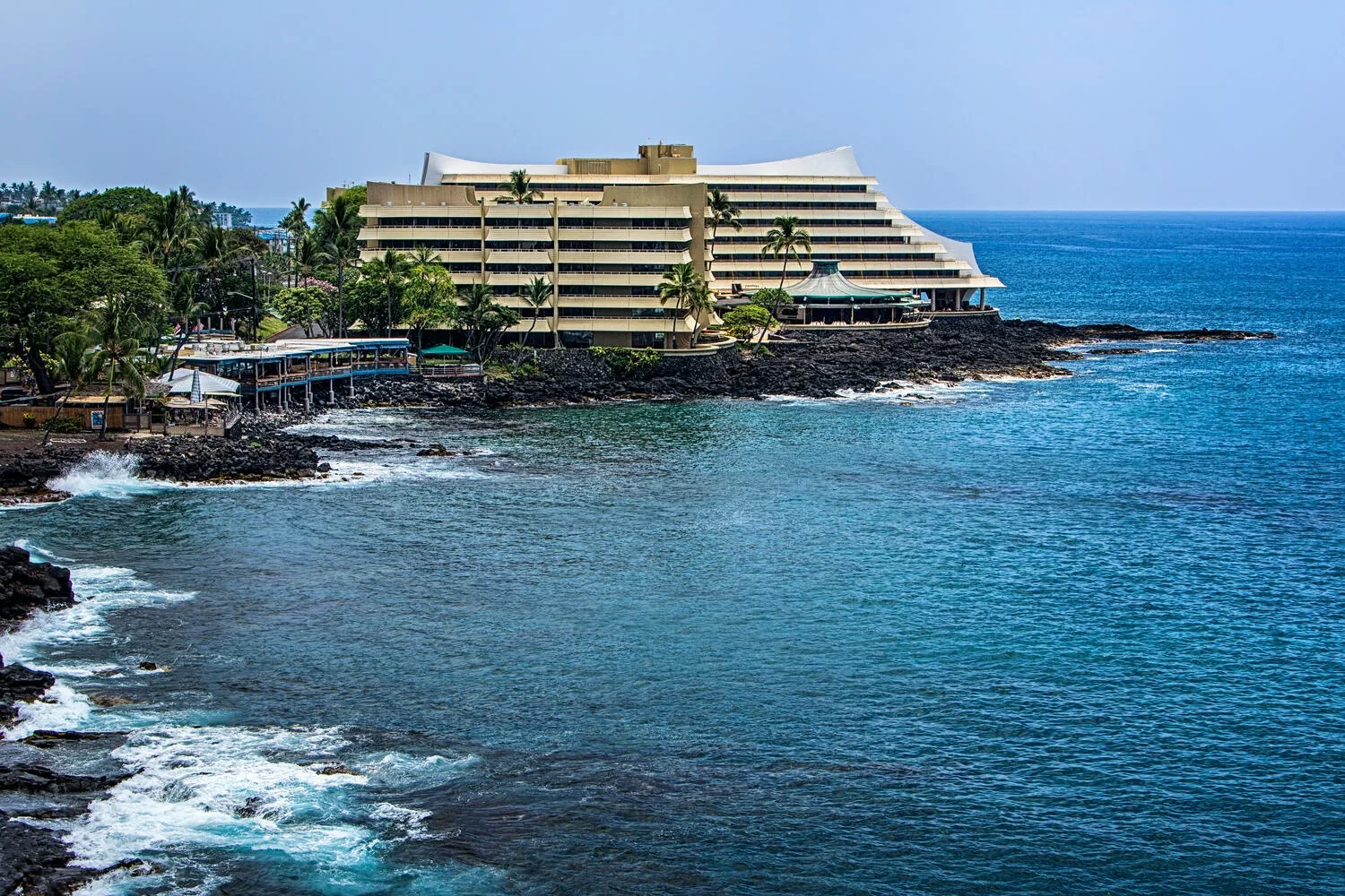 Un hotel costero se encuentra junto a una costa rocosa y aguas azules.