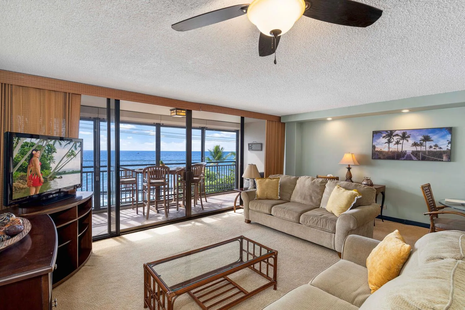 Una sala de estar con asientos, un televisor y puertas corredizas de vidrio con vista al mar.