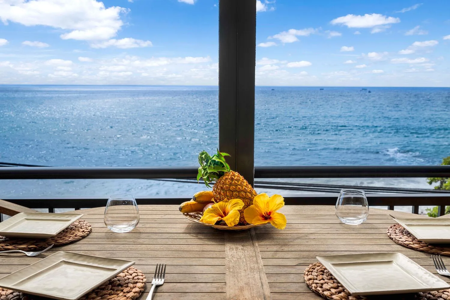 Una mesa puesta con platos y fruta tropical da al mar.