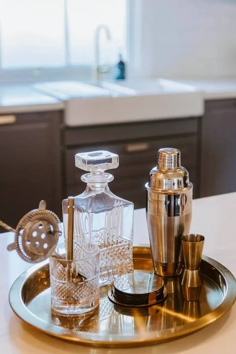 A bar tray with a glass decanter and metal cocktail shaker sits on a counter.