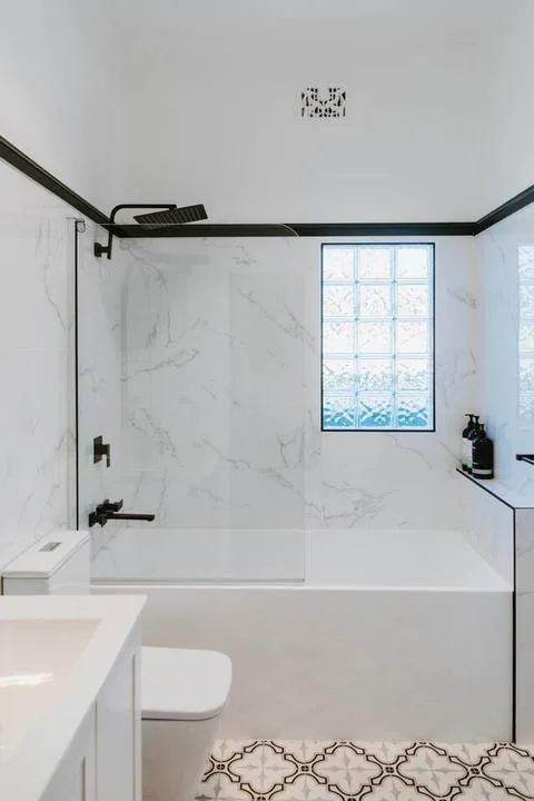 A bright bathroom with a bathtub, glass shower panel, and patterned floor tiles.