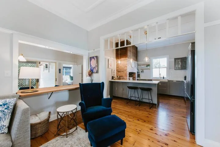 An open-plan living area with a kitchen, bar seating, and a dark lounge chair.