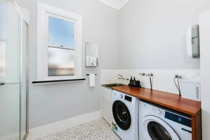 A laundry room with two washing machines beneath a wooden countertop.