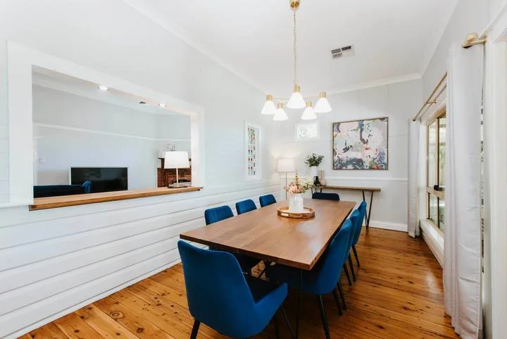 A bright dining room with a wooden table and blue seating beneath a chandelier.