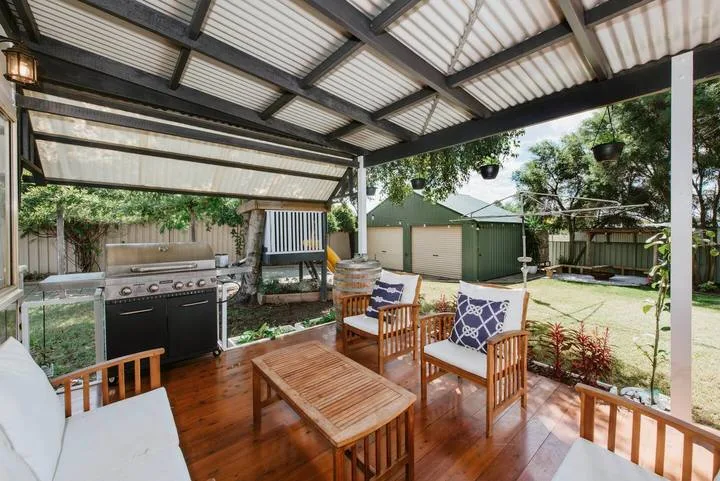A covered outdoor patio with wooden seating overlooks a fenced yard.
