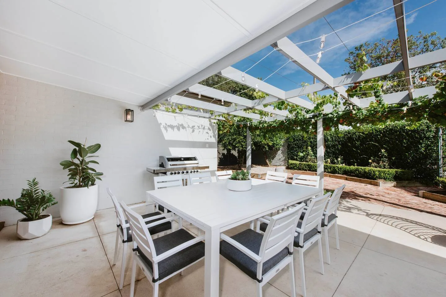 Una zona cubierta de comedor al aire libre, con mesa y barbacoa, da a un jardín.