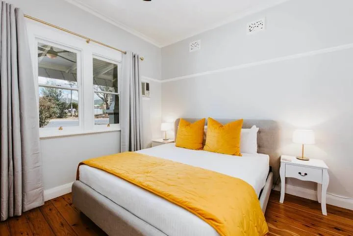 A bedroom with a bed dressed in white and bright yellow bedding.
