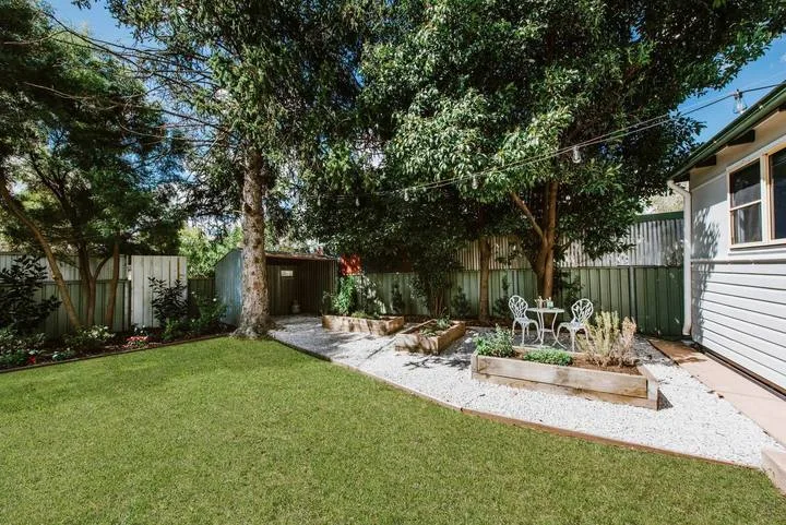 A landscaped yard with a lawn, gravel path, garden beds, and outdoor seating.
