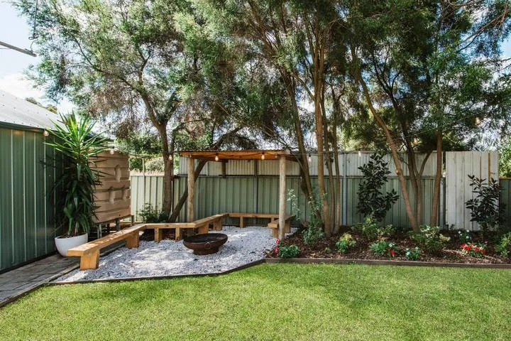 A shaded garden seating area with a wooden bench beside a small fire pit.