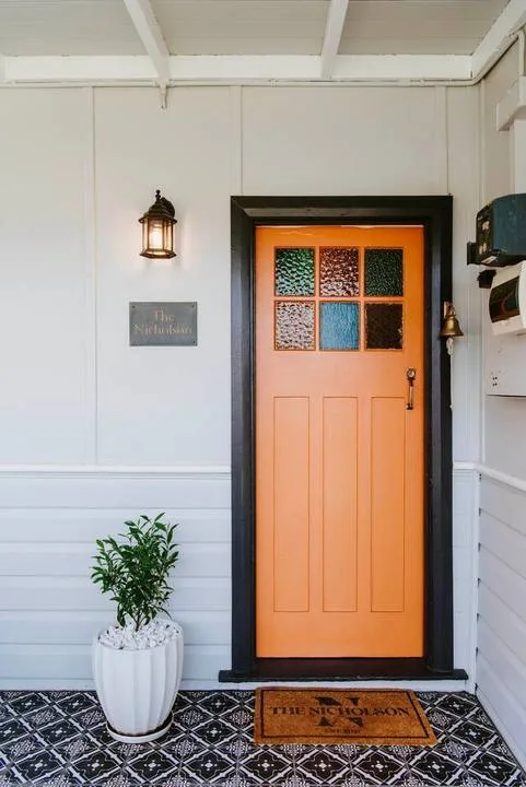 An orange entrance door with glass panes stands beside a potted plant.