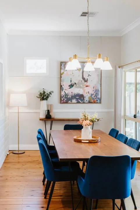 A dining room with a wooden table, blue seating, and an abstract painting.