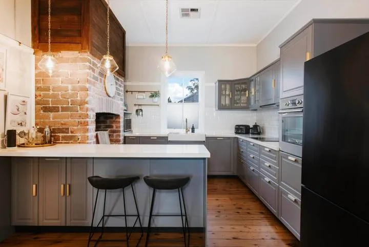 A modern kitchen with gray cabinets, a central island, and brick accents.