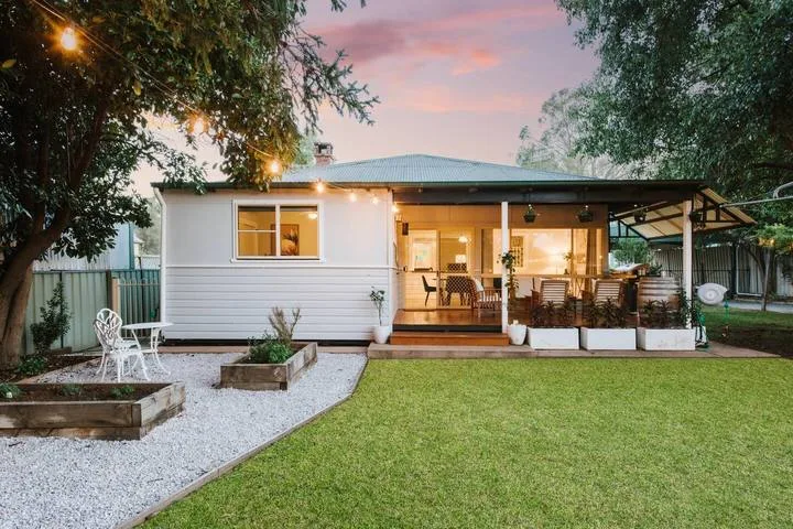 A house with a covered patio opens onto a lawn and gravel seating area.