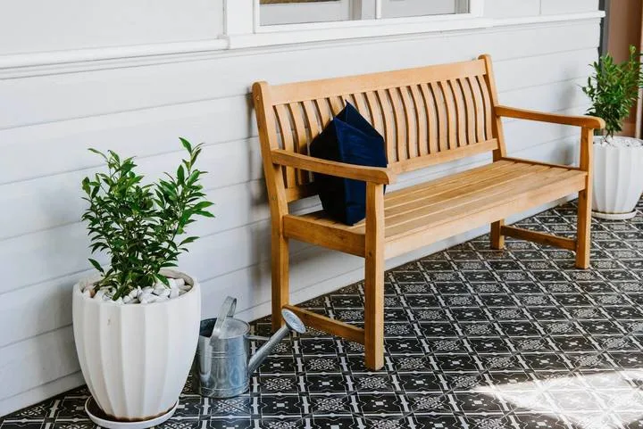 A wooden bench sits on a tiled porch beside potted plants.