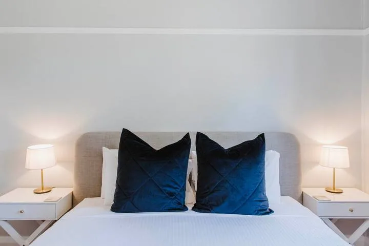 A bedroom with a neatly made bed, dark pillows, and matching bedside lamps.