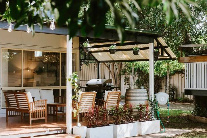 A garden patio with outdoor seating beneath a shaded pergola.