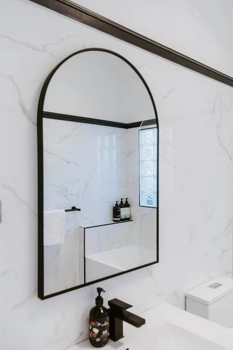 A bathroom vanity with an arched mirror, wall-mounted faucet, and marble-look walls.