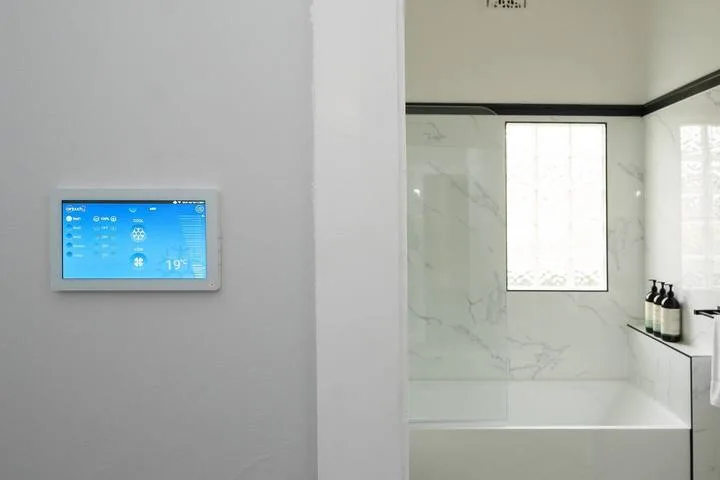 A bright bathroom with a bathtub, window, and wall-mounted control panel.