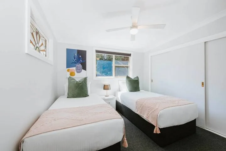 A bright bedroom with two beds, pale bedding, and a window.