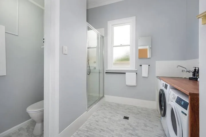 A bright bathroom with a glass shower and laundry machines.