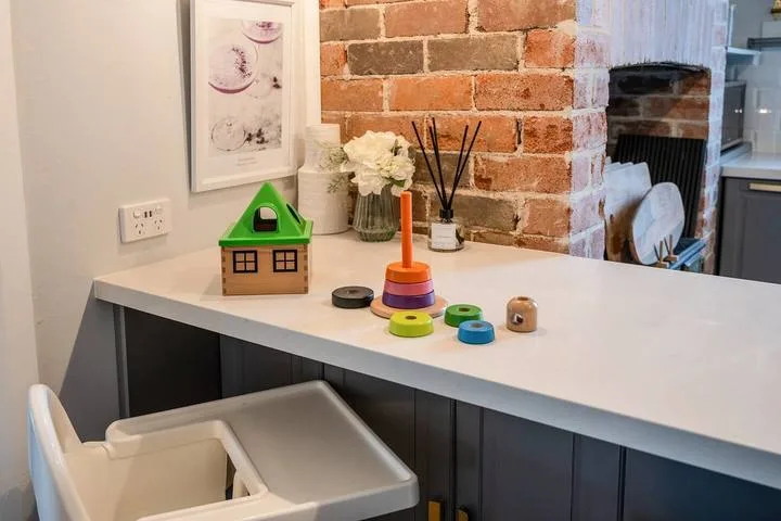 A kitchen counter with colorful toys and flowers beside an exposed brick wall.