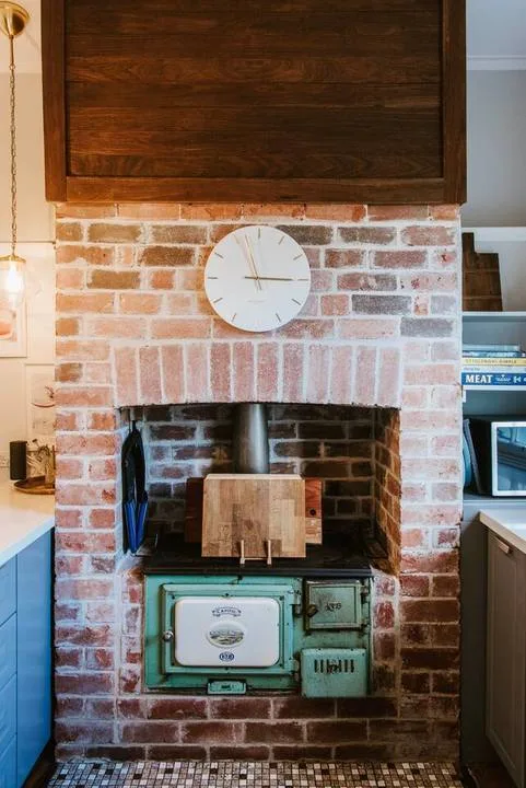 A brick fireplace with a vintage green stove and a clock above it.