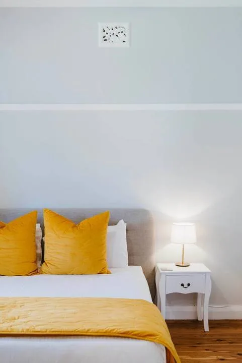 A bedroom with yellow bedding and a bedside table with a lamp.