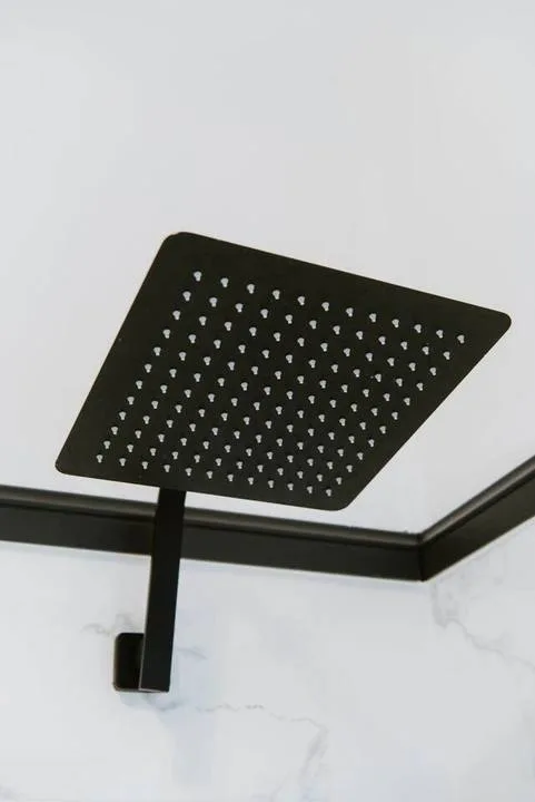 A black showerhead is mounted against a light marble-patterned wall.