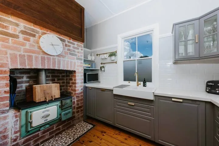 A kitchen with a brick fireplace, sink, and cabinets.
