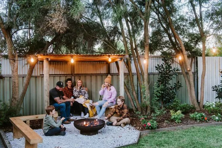 An outdoor patio with people gathered around a fire pit beneath string lights.