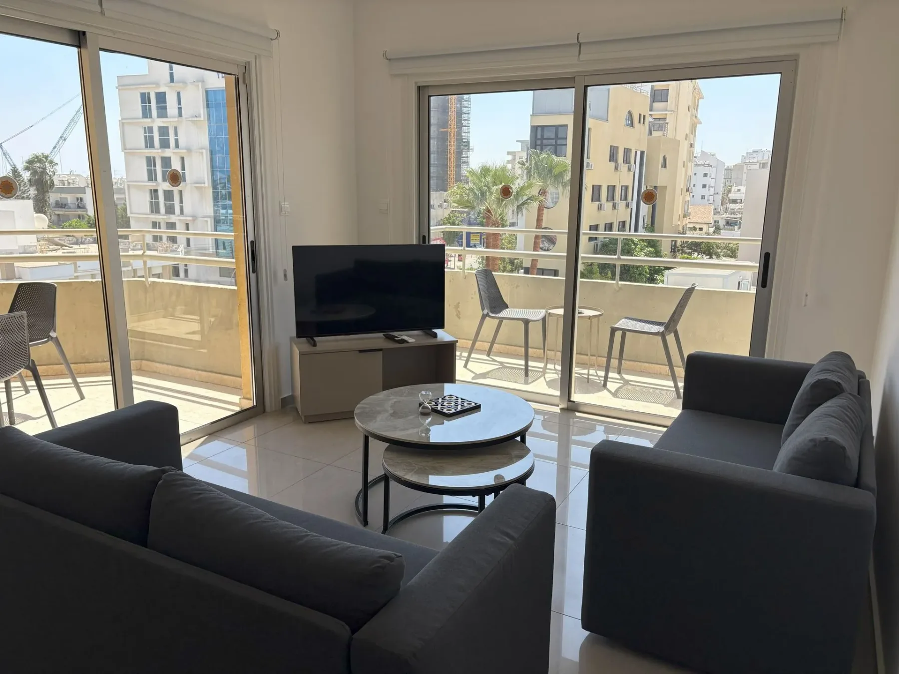 Sala de estar con sillón, mesas de centro, televisor y balcón con vistas a la ciudad y al mar.