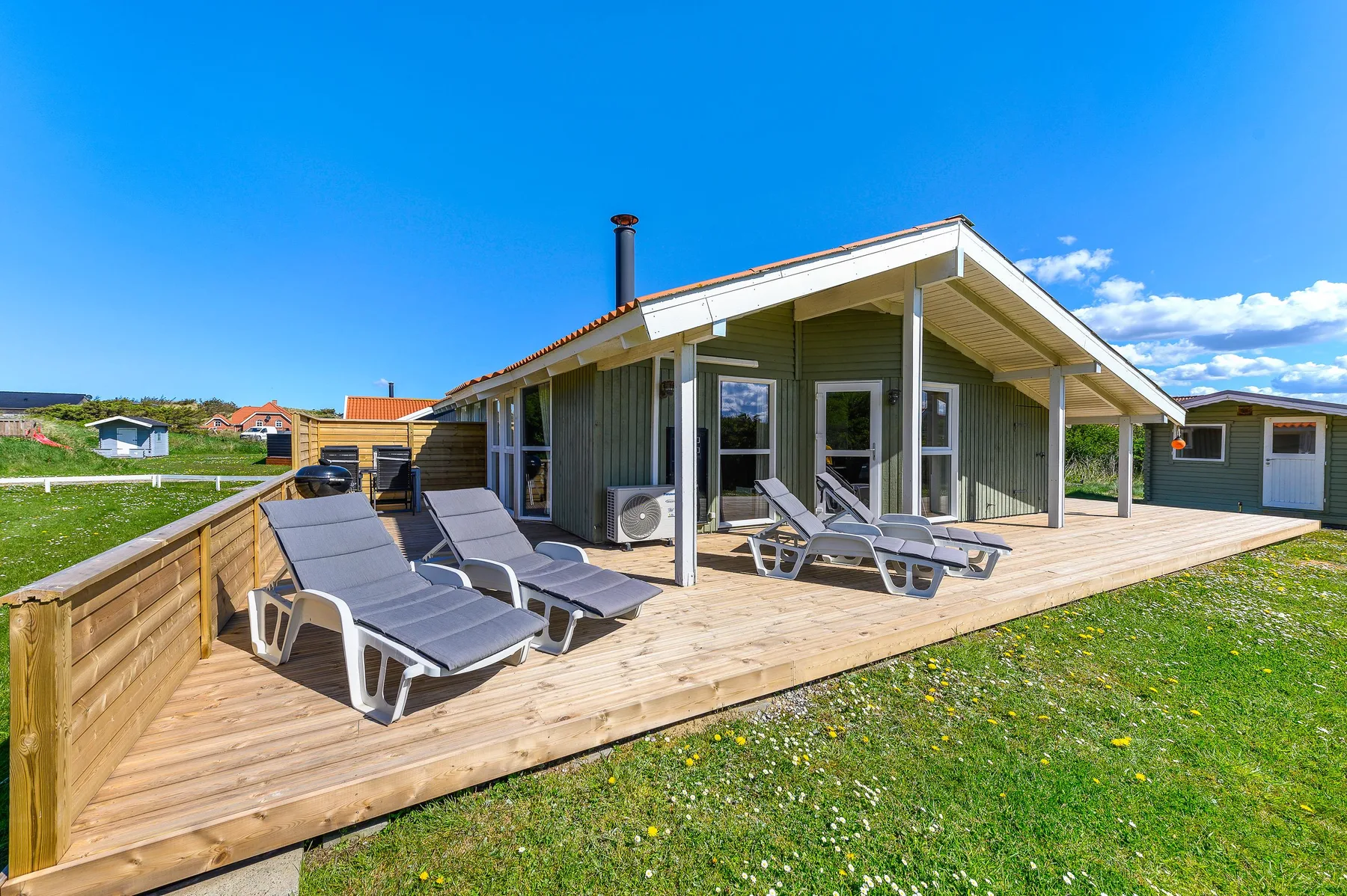 Una casa moderna con una terraza de madera y asientos al aire libre bajo un cielo despejado.