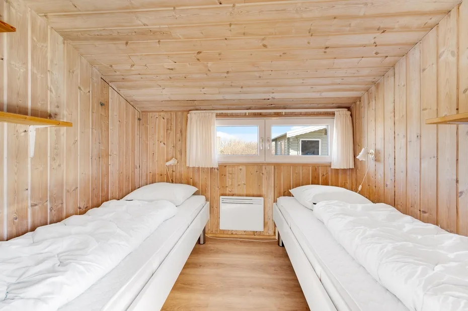 Un dormitorio revestido de madera con dos camas y una ventana.