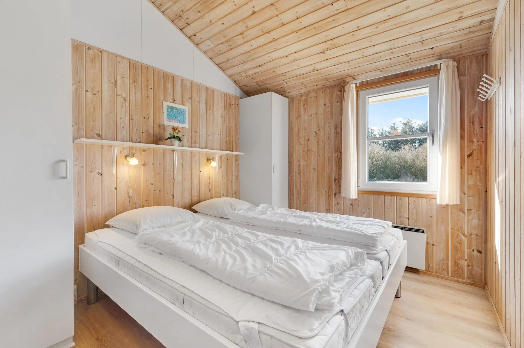 Un dormitorio luminoso con una cama doble bajo un techo inclinado de madera.