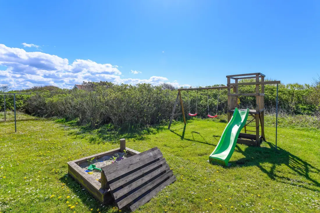 Zona de juegos al aire libre con césped, un tobogán, columpios y arenero.