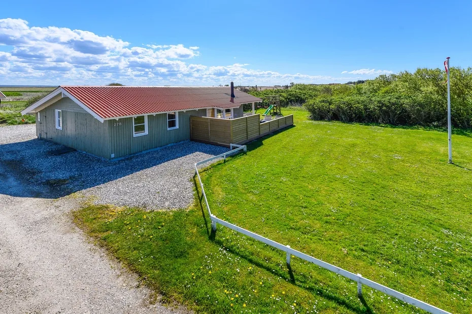 Una casa pequeña se encuentra junto a un amplio césped verde bajo un cielo azul.