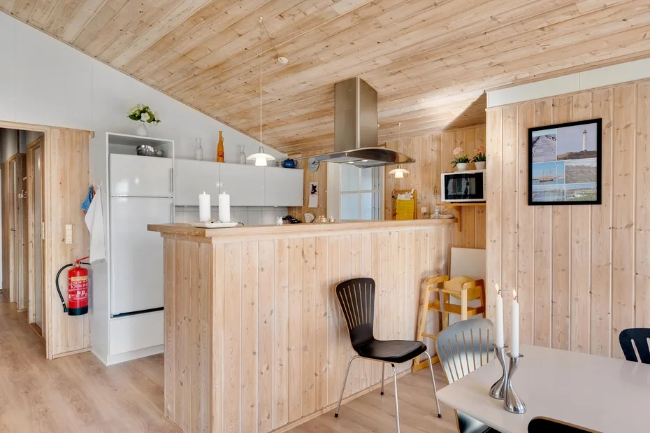 Cocina y comedor revestidos de madera, con una barra central y una mesa.