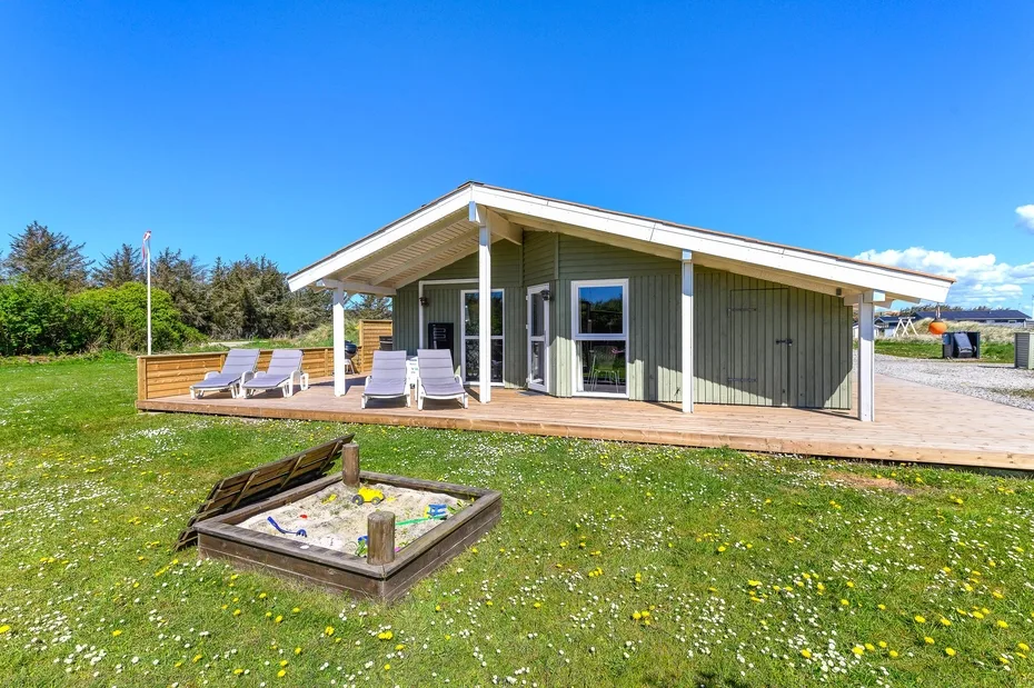 Una casa moderna y baja está junto a una terraza de madera con asientos al aire libre y césped.